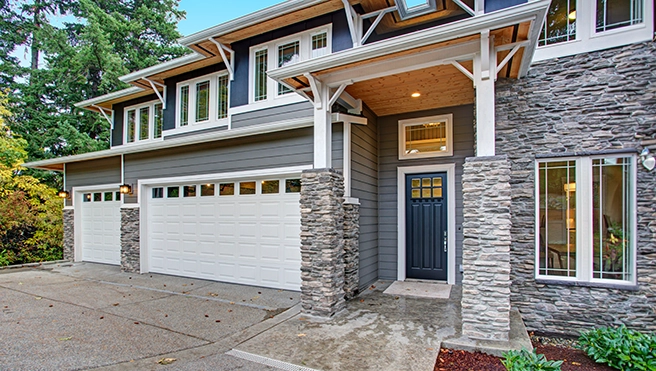 House with a two-door garage and trees on the side.