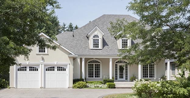 House with a two-door garage and a tree in the front yard.