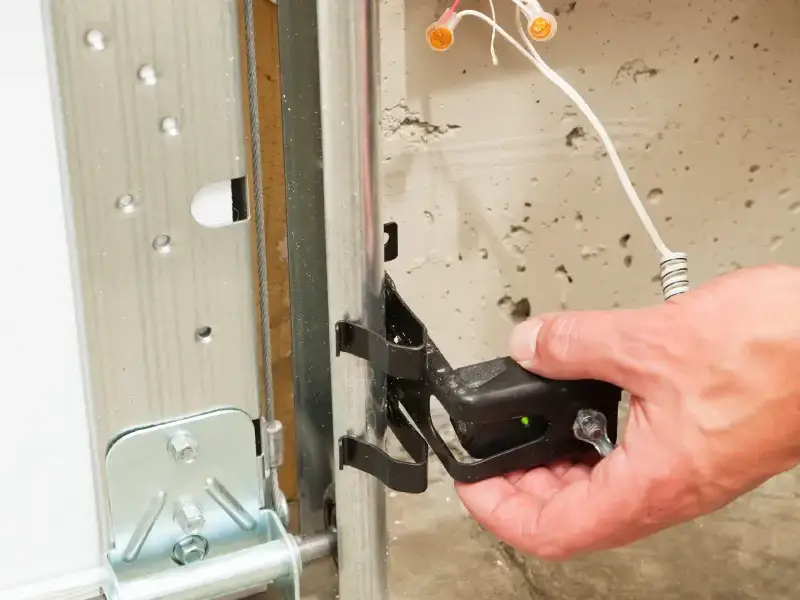 A service professional adjusts a garage door safety eye.