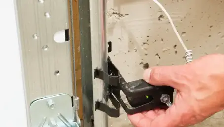 A service professional adjusts a garage door safety eye.