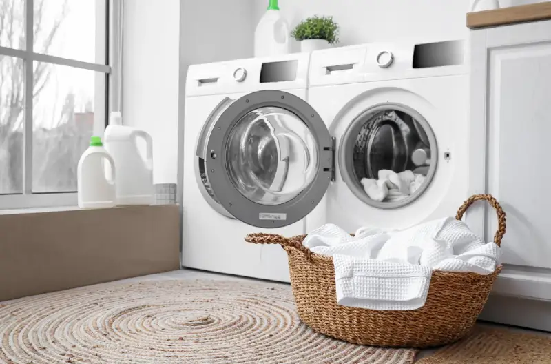 A laundry room containing a washing machine, dryer, and laundry basket in a remodeled garage. 